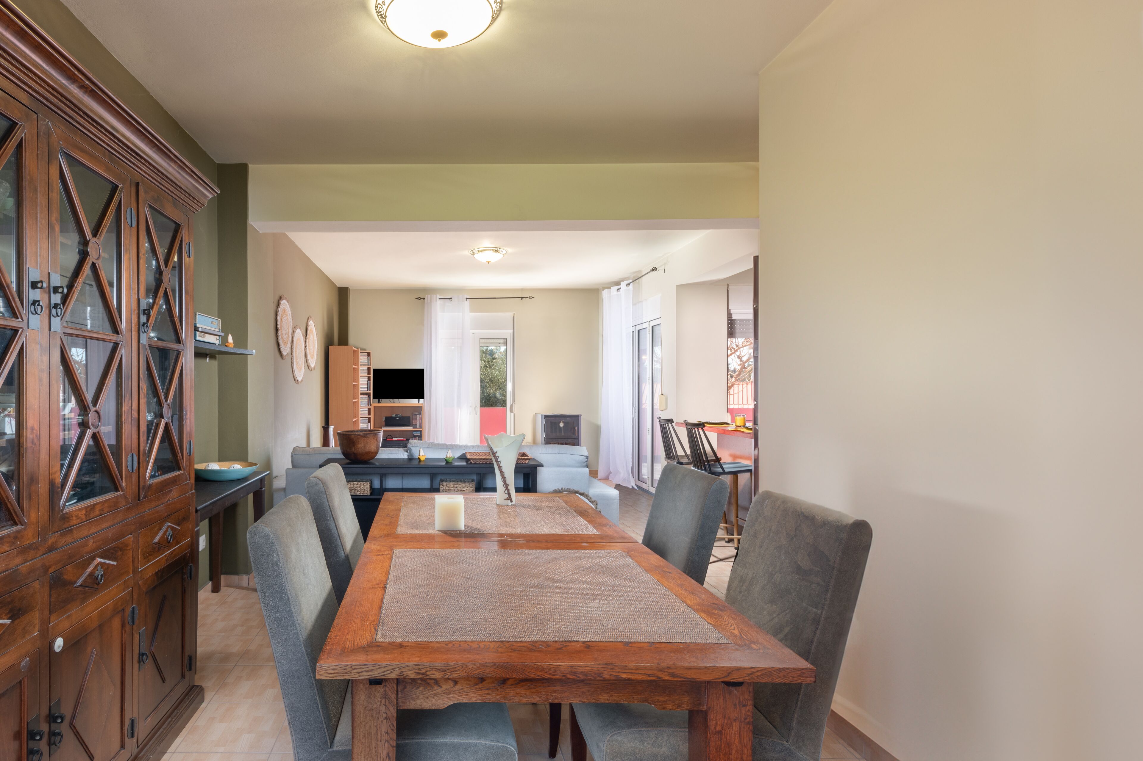 A dining area with a wooden table and chairs, a cabinet with glass doors, and a television in the background.