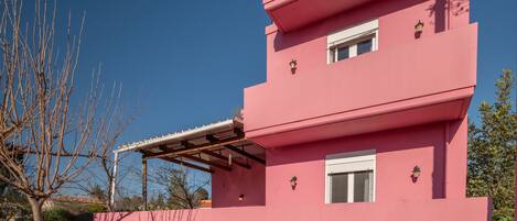 A pink two-story building with a covered patio area and a small garden.