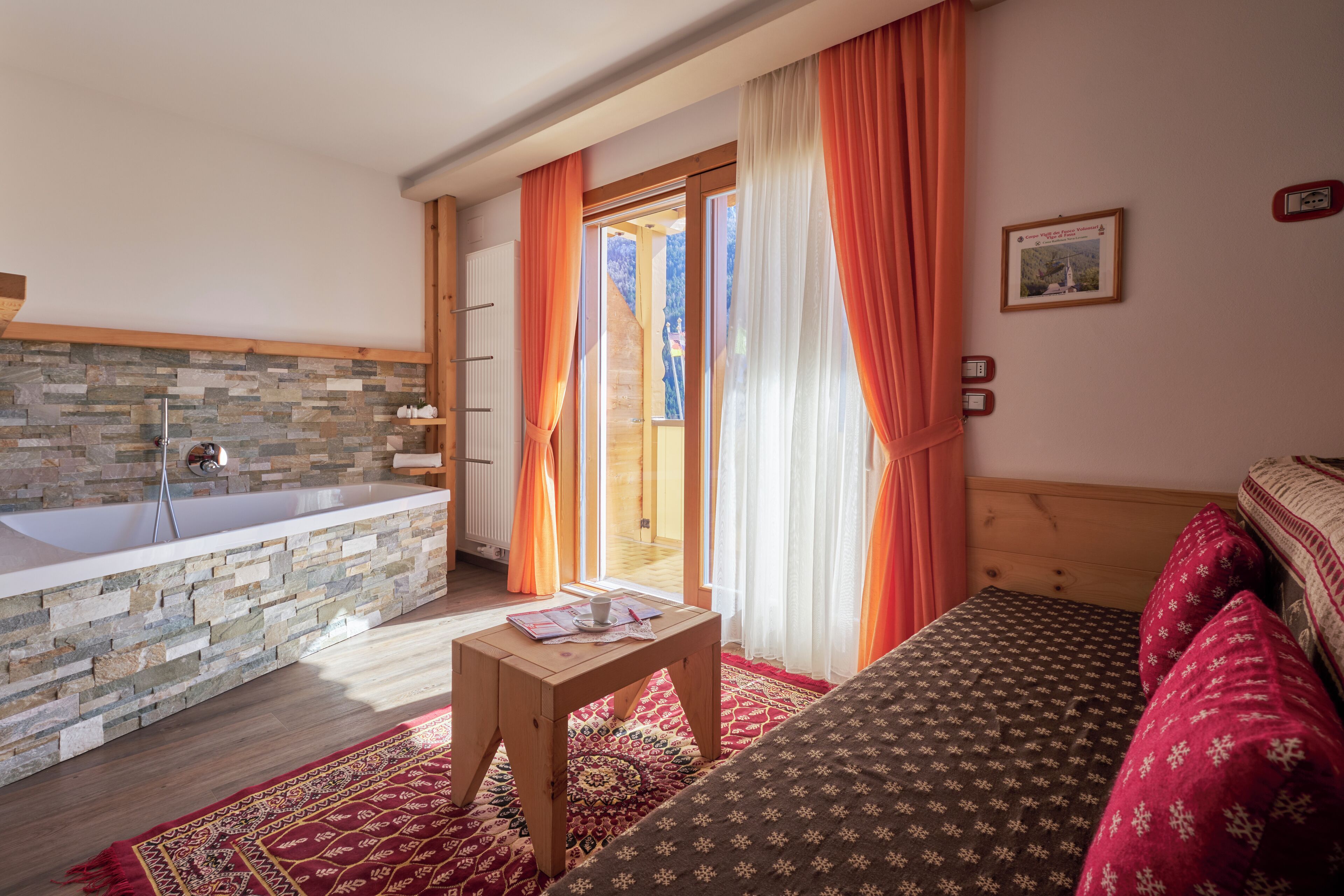 A room with a stone wall, a bathtub, a wooden bed, and a red patterned rug.