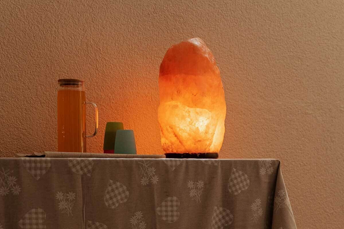 A table with a salt lamp, a glass pitcher, and candles.