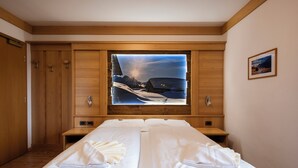 Una habitación de hotel con dos camas, paneles de madera, un ventanal con vistas panorámicas y un cuadro en la pared.