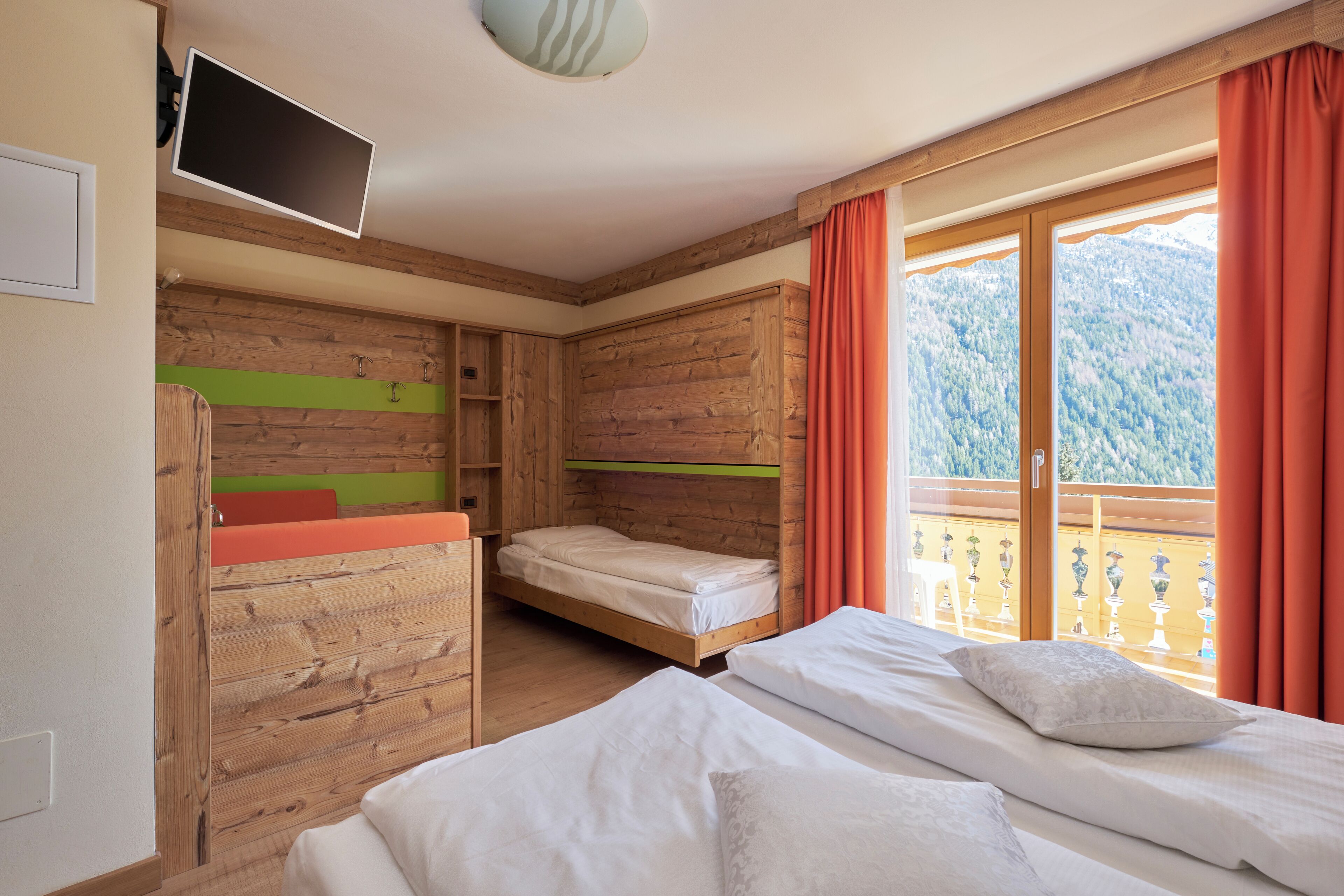 A room with wooden walls, a bed, a bunk bed, and a TV.
