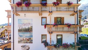 Un edificio de varios pisos con balcones decorados con flores, una pintura de paisaje de montaña y una cesta de pan.