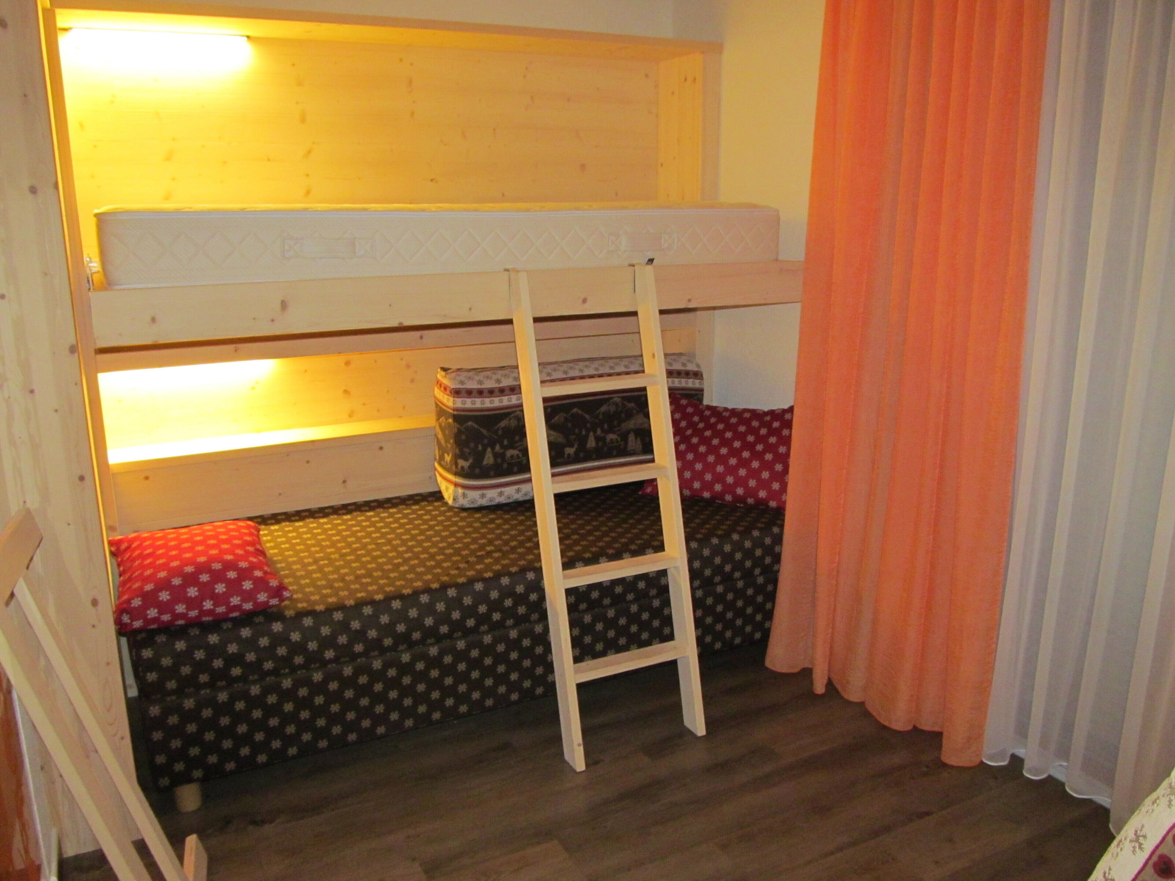 A bunk bed with a ladder, a small storage box, and a patterned pillow.