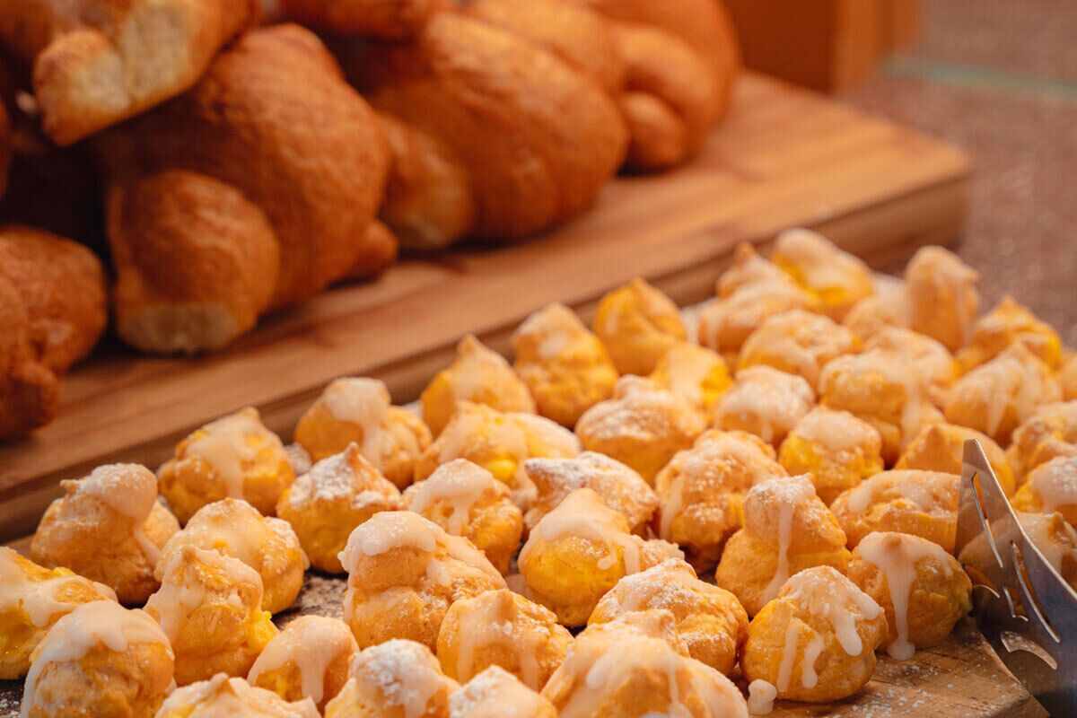 A tray of cream puffs with powdered sugar and a wooden board in the background.