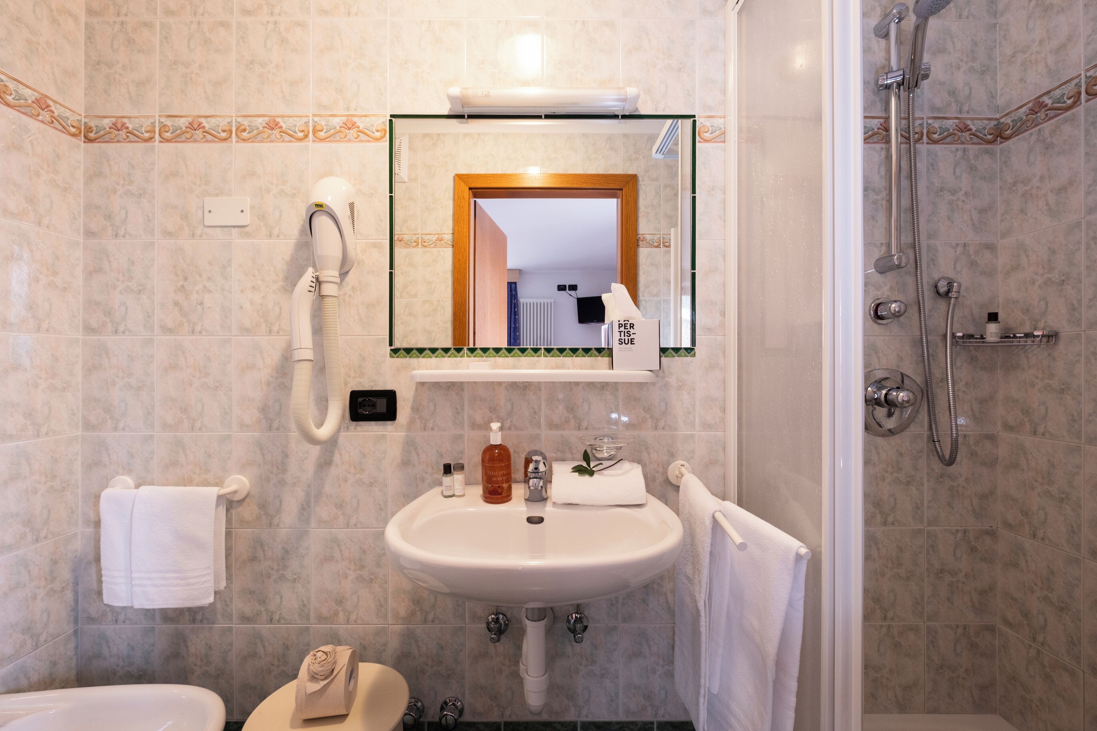 Un baño con lavamanos, espejo, toallero, ducha e inodoro.