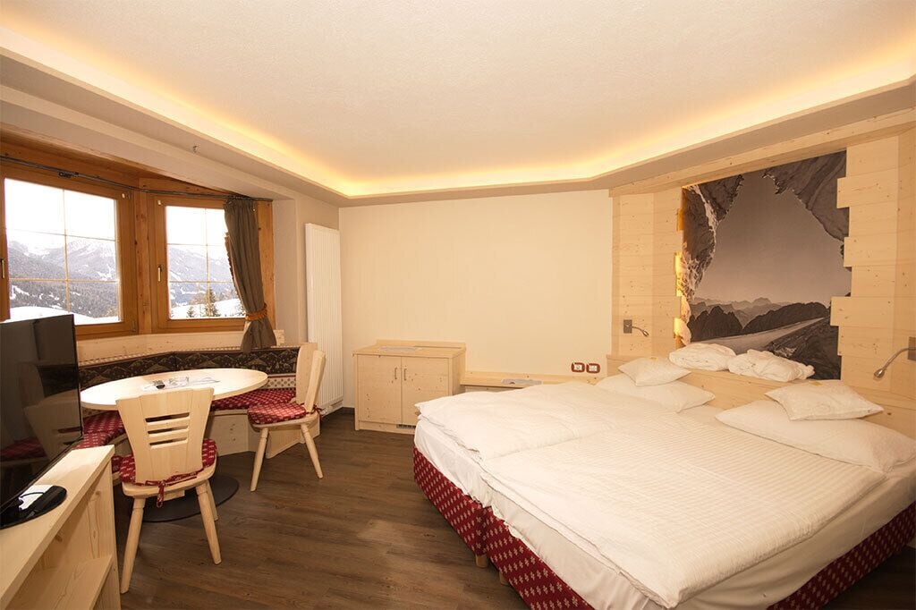A hotel room with a large bed, a desk with a chair, a small cabinet, and a window with a view of mountains.