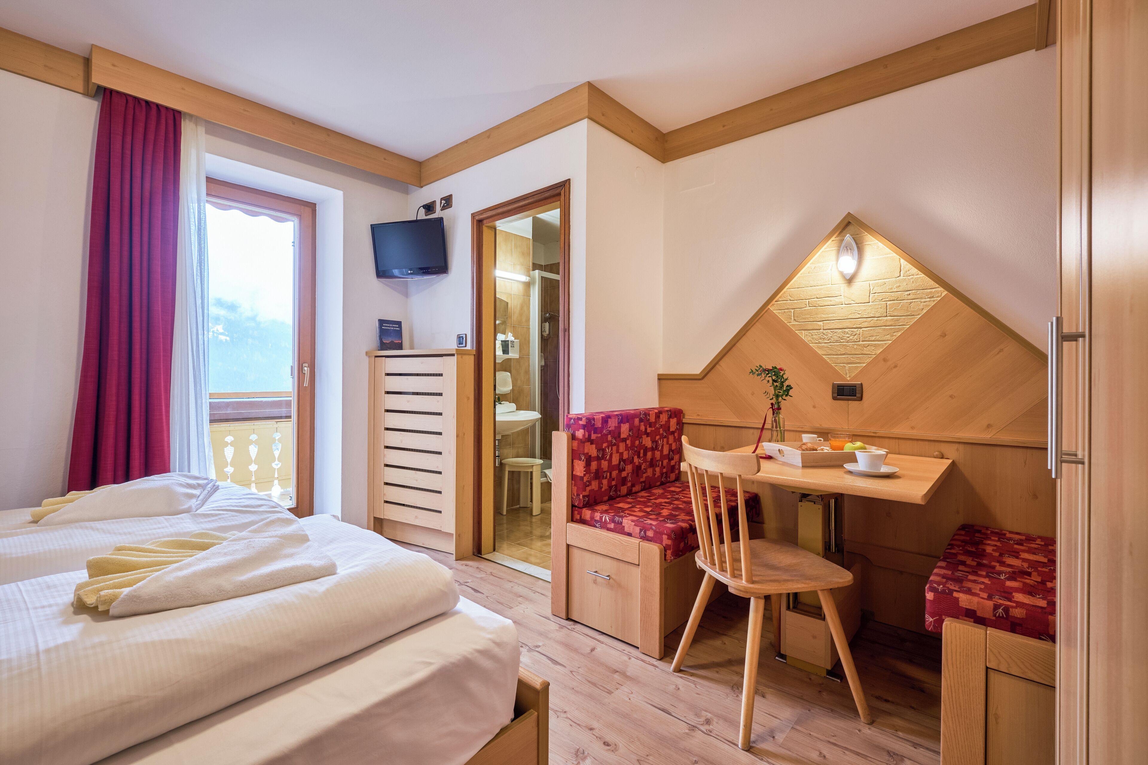 A hotel room with a bed, a desk, a chair, a TV, and a bathroom visible through an open door.