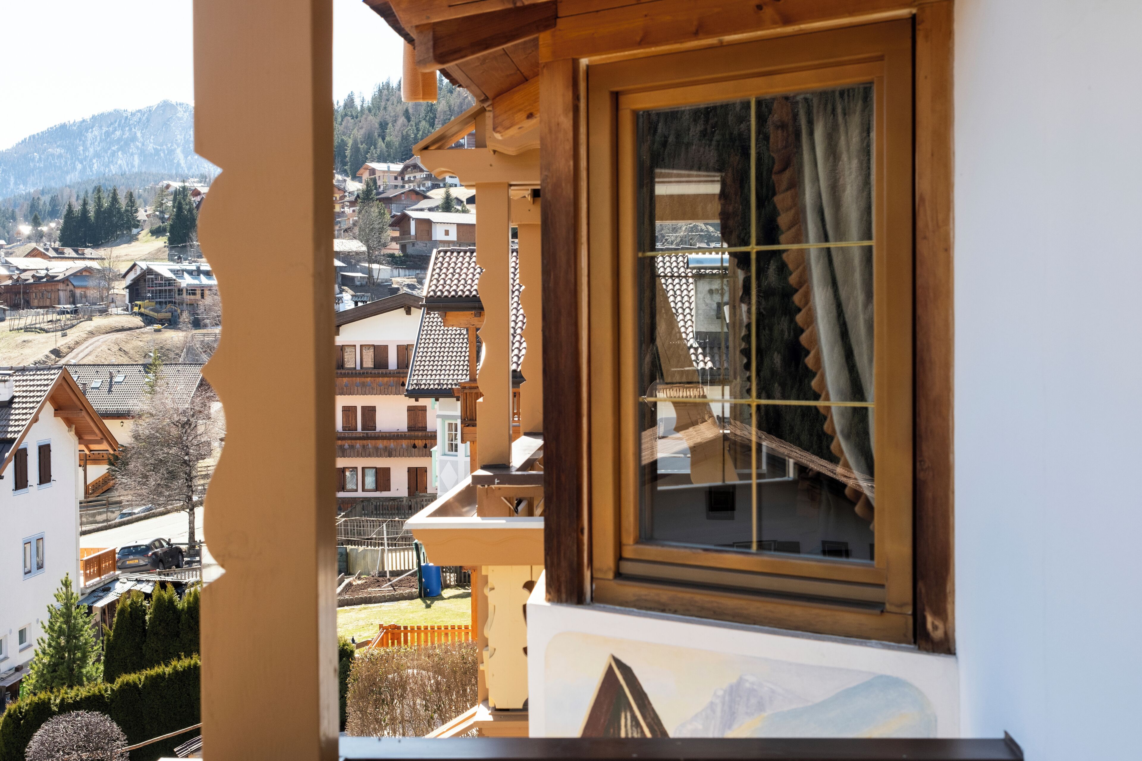 A view from a window with a wooden frame and a curtain, overlooking a town with traditional buildings and a mountain in the background.