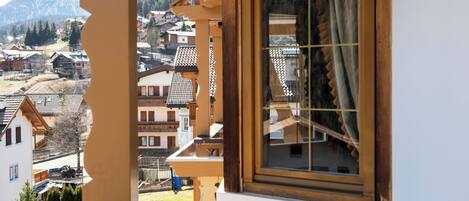 A view from a window with a wooden frame and a curtain, overlooking a town with traditional buildings and a mountain in the background.