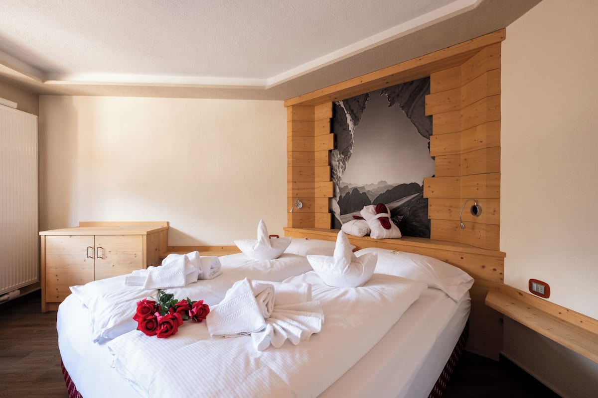 Een hotelkamer met een groot bed, een houten hoofdbord, een schilderij en een houten dressoir.
