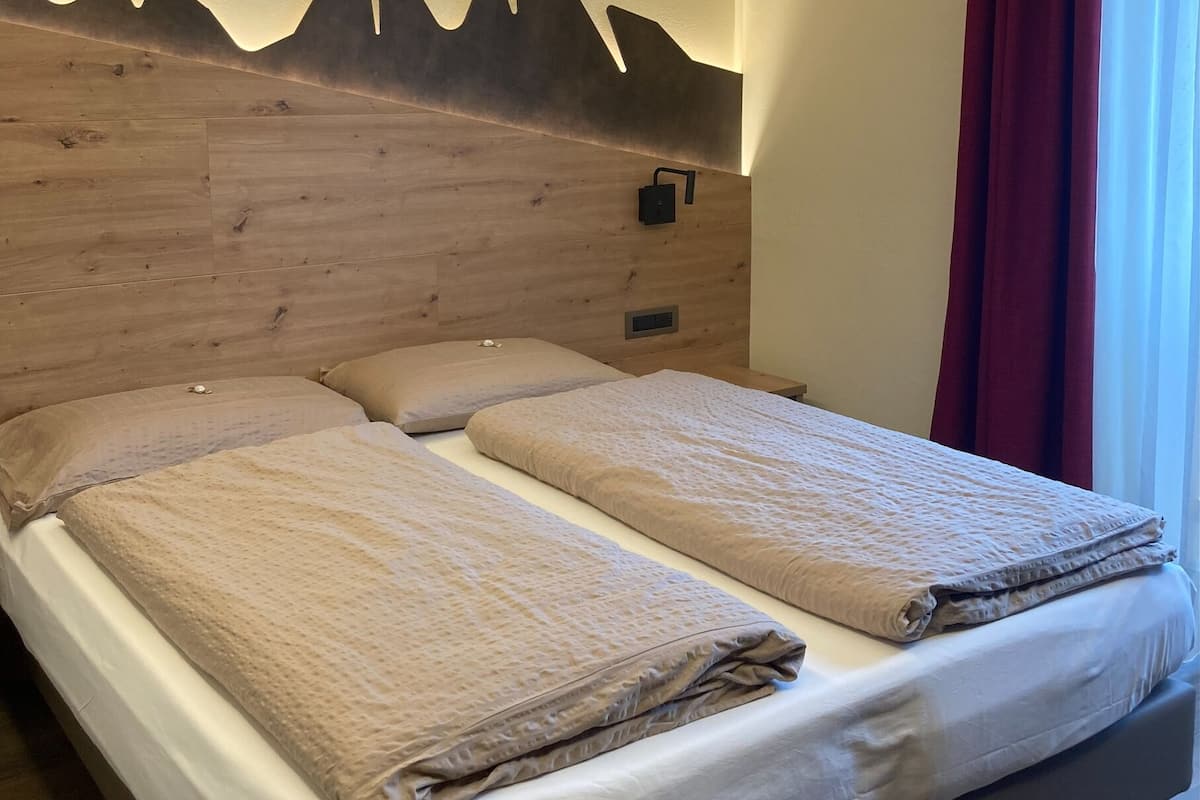 Een tweepersoonsbed met houten hoofdbord, twee kussens en een dekbed.