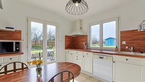Une cuisine moderne avec des armoires blanches, un plan de travail en bois, un four à micro-ondes encastré et un lave-vaisselle. On y trouve une table à manger avec des chaises et un vase rempli de fleurs.