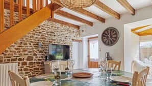 Un coin repas agrémenté d’un mur en pierre, de poutres en bois, d’une grande horloge et d’une table dressée pour quatre personnes.