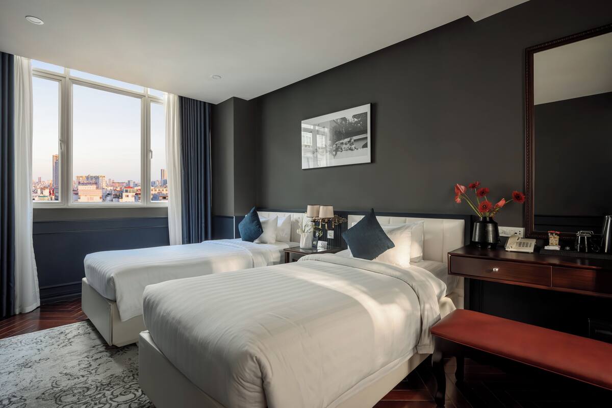 Habitación de hotel con dos camas, un escritorio, un espejo y vistas a la ciudad.