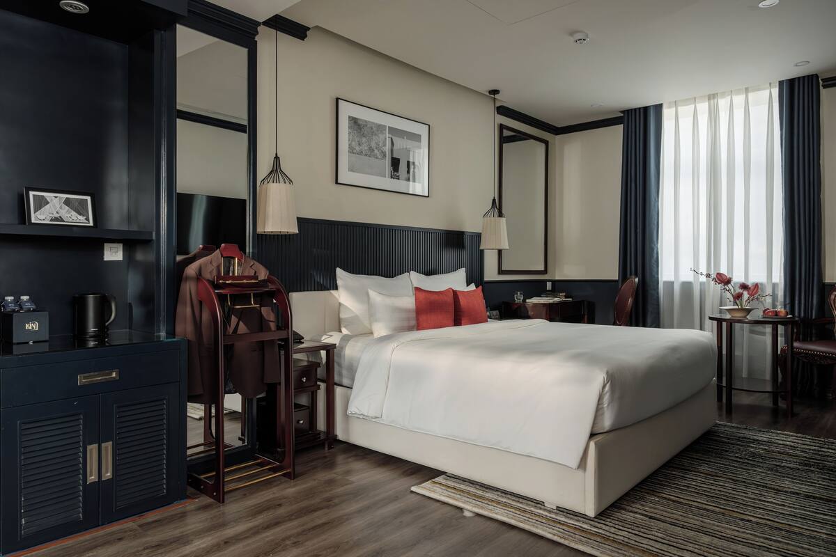 Una habitación de hotel moderna con una cama grande, un escritorio, un armario y un espejo.