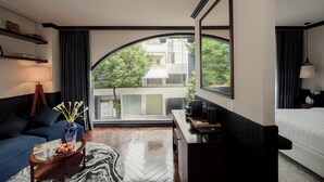 A modern hotel room with a large arched window, a sofa, a coffee table with a vase, a desk with a lamp, and a bed. - Kin Hotel Dong Du (Ho Chi Minh City)