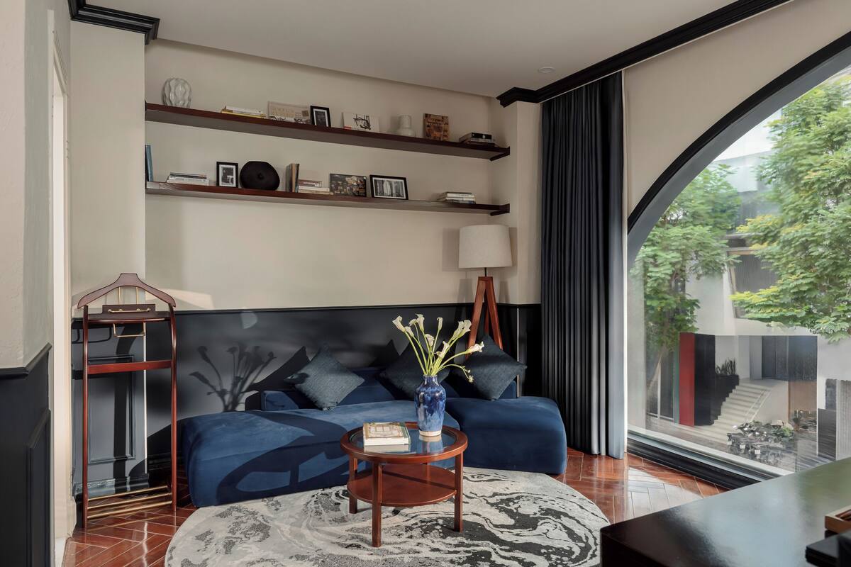 Una sala de estar moderna con un sofá azul, una mesa de centro redonda de madera y un ventanal con vistas a un jardín.
