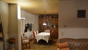 A dining area with a table set for four, surrounded by wooden chairs. There is a patterned rug on the floor, a radiator under the window, and a lamp beside the window. - Ferienwohnung Miezal, 1-4 Pers (Raesfeld)