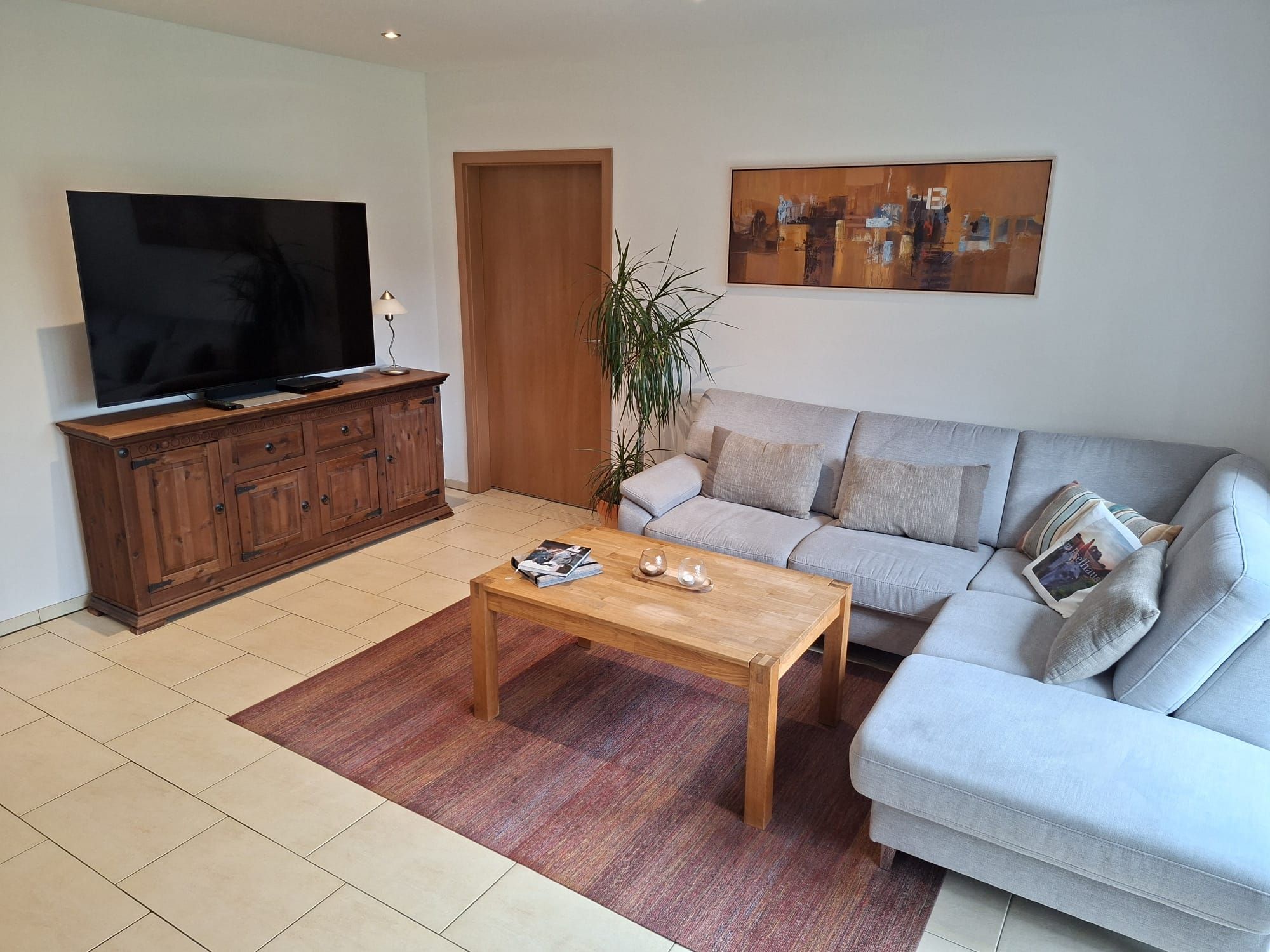 Ein Wohnzimmer mit Flachbildfernseher, Holzschrank, Sofa, Couchtisch und einem Gemälde an der Wand.