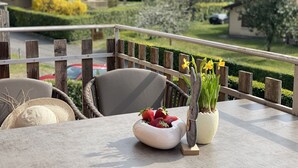 A balcony with a table set for dining, featuring a bowl of strawberries and a vase with daffodils.