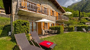 A stone building with a balcony, outdoor seating, and a grassy lawn.