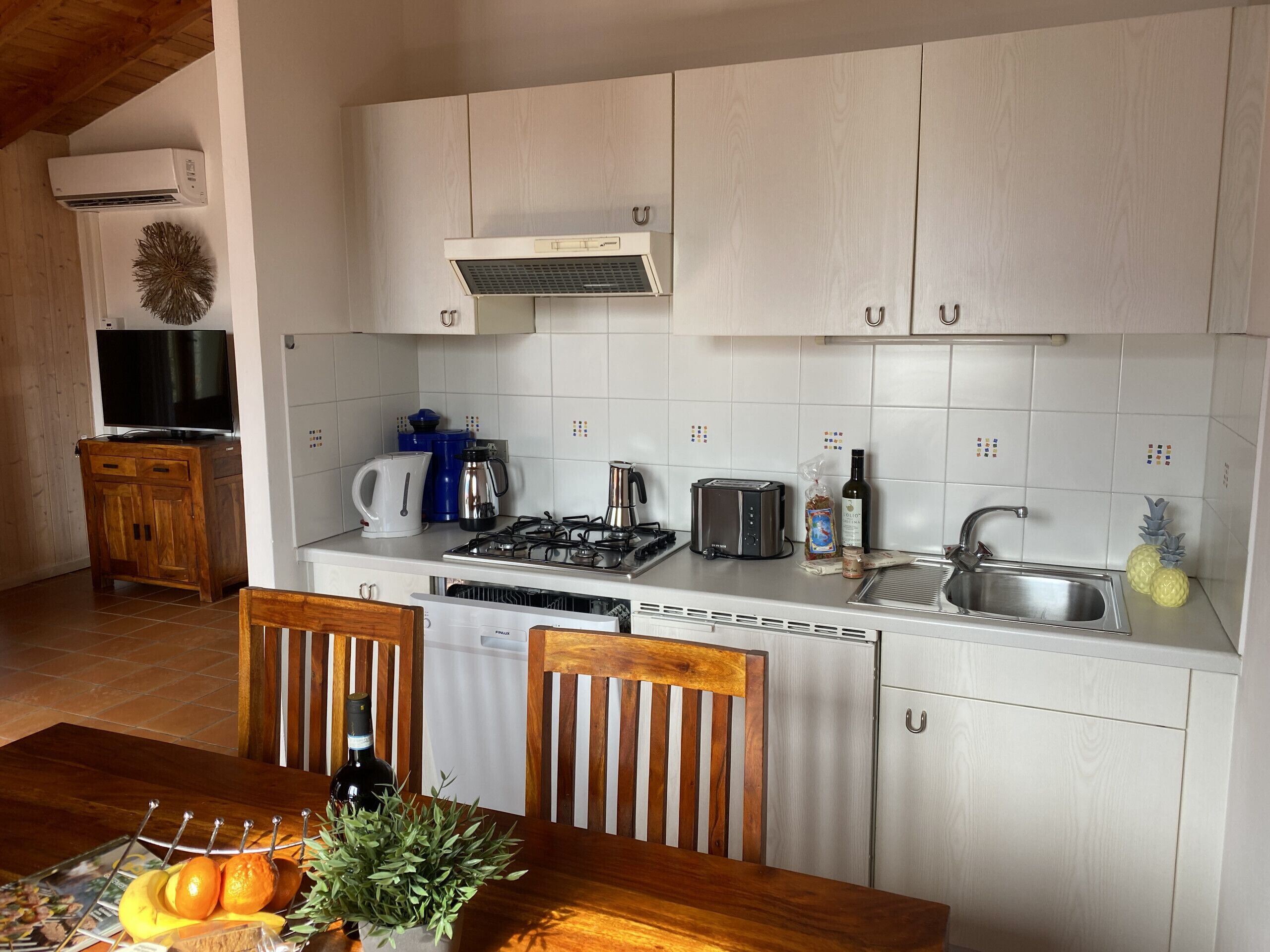 Cocina compacta con armarios blancos, estufa, lavaplatos y una zona de comedor con mesa y sillas.