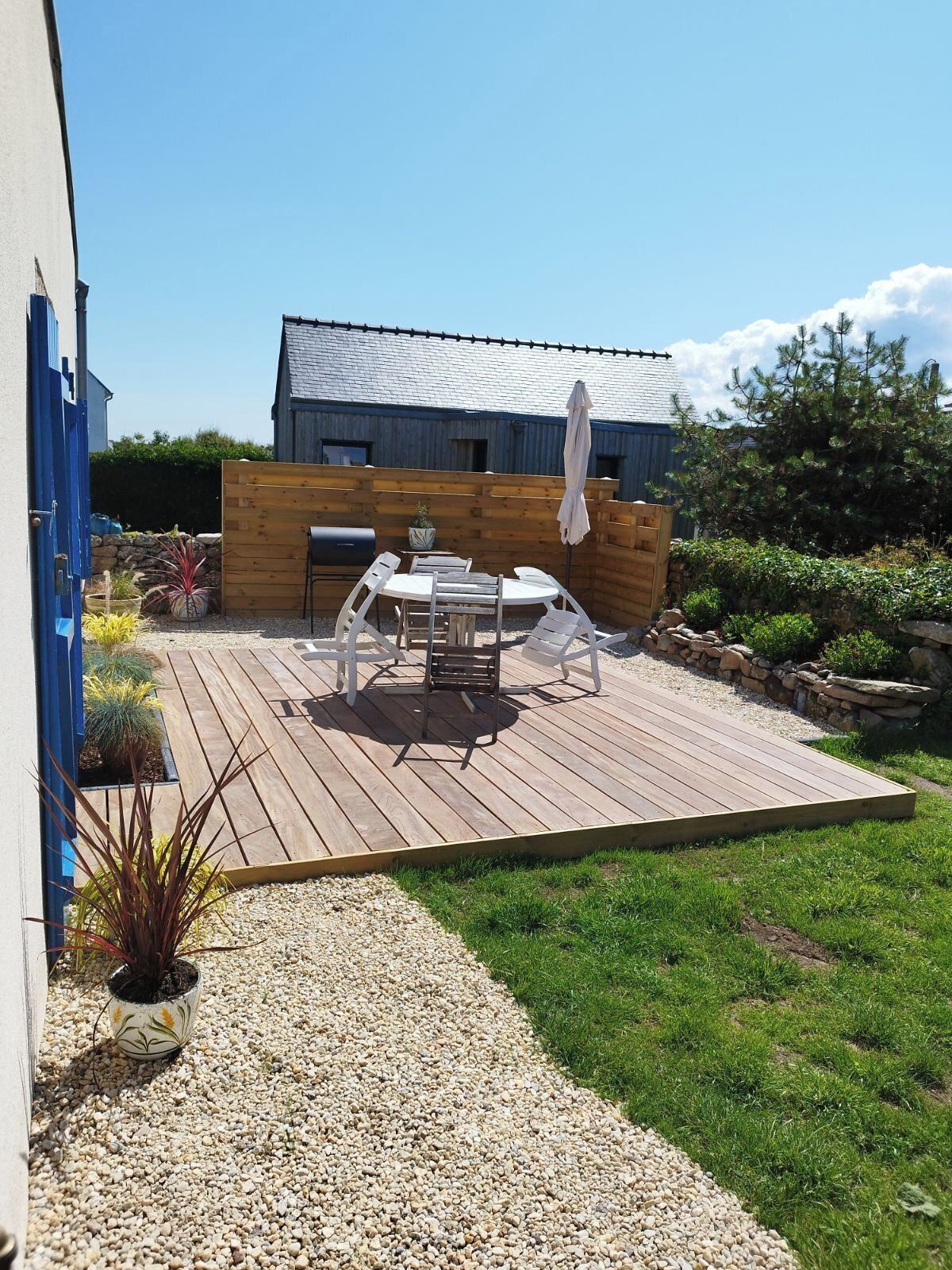 Une terrasse en bois avec des meubles d’extérieur, un barbecue et un mur en pierre.