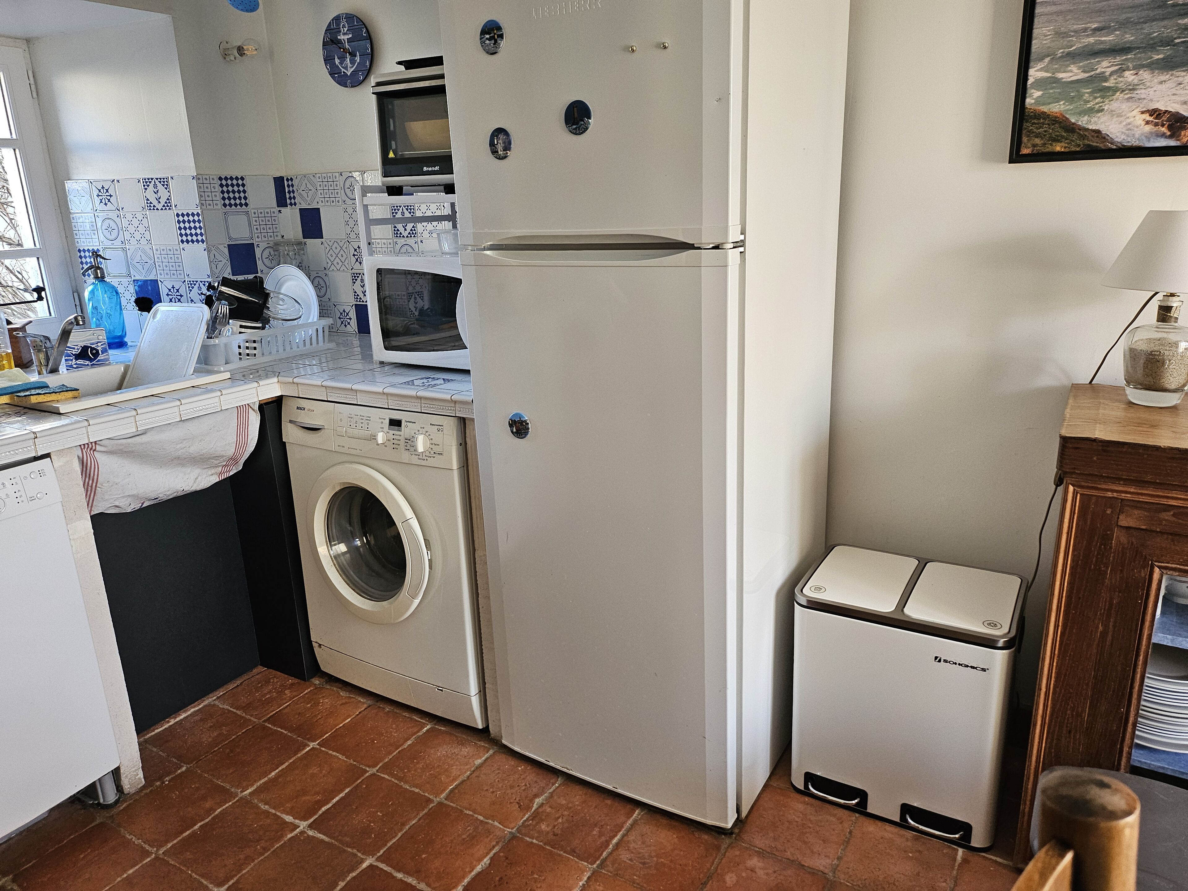 A compact kitchen with a washing machine, a small refrigerator, and a microwave.