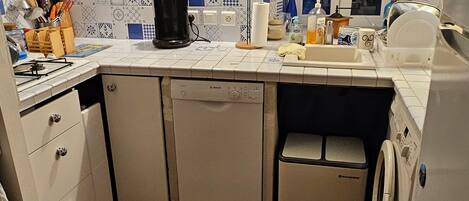 Une cuisine compacte avec des meubles blancs, un lave-vaisselle Bosch, un lave-linge et une fenêtre offrant une belle vue.
