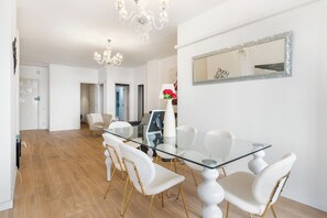 Un espace de salle à manger moderne avec une table en verre, des chaises blanches et un lustre.