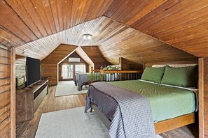 A cozy attic bedroom with a sloped ceiling, a bed with green bedding, a wooden bench, and a television.