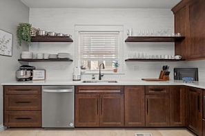 Una cocina con armarios de madera, lavavajillas y ventana con persianas.
