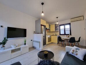 Un appartement moderne doté d’une télévision à écran plat, d’un coin repas avec une table et des chaises, d’une cuisine équipée d’une cuisinière et d’un réfrigérateur, et d’un salon avec un canapé et une table basse.