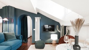 Un salon moderne avec un canapé bleu, une petite table ronde sur laquelle est posé un vase, et un téléviseur fixé au mur.