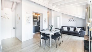 Amplia sala de estar con una mesa de comedor para cuatro personas, un sofá de cuero oscuro y una cocina al fondo.