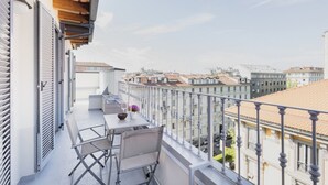 Un balcón con mesa y sillas, con vistas a un paisaje urbano de edificios y un cielo despejado.