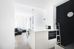 Efficient living space with a central island kitchenette, black clock, and comfortable seating area.