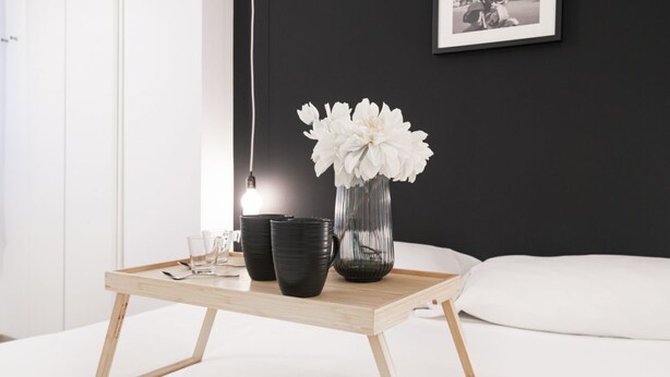 Una habitación moderna con una mesa de centro de madera, tazas blancas y negras, un jarrón de vidrio con flores blancas y una fotografía en blanco y negro enmarcada en la pared.