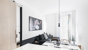 Una sala de estar moderna con un sofá negro, una mesa de comedor para dos personas y un ventanal grande.