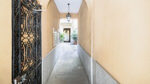 Un pasillo estrecho con una reja de hierro decorativa, suelo de piedra y una lámpara en el techo.