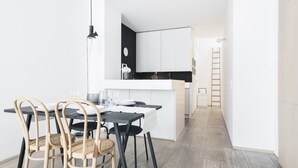 Una cocina moderna con armarios blancos, encimera negra y un comedor con mesa negra y sillas de mimbre.