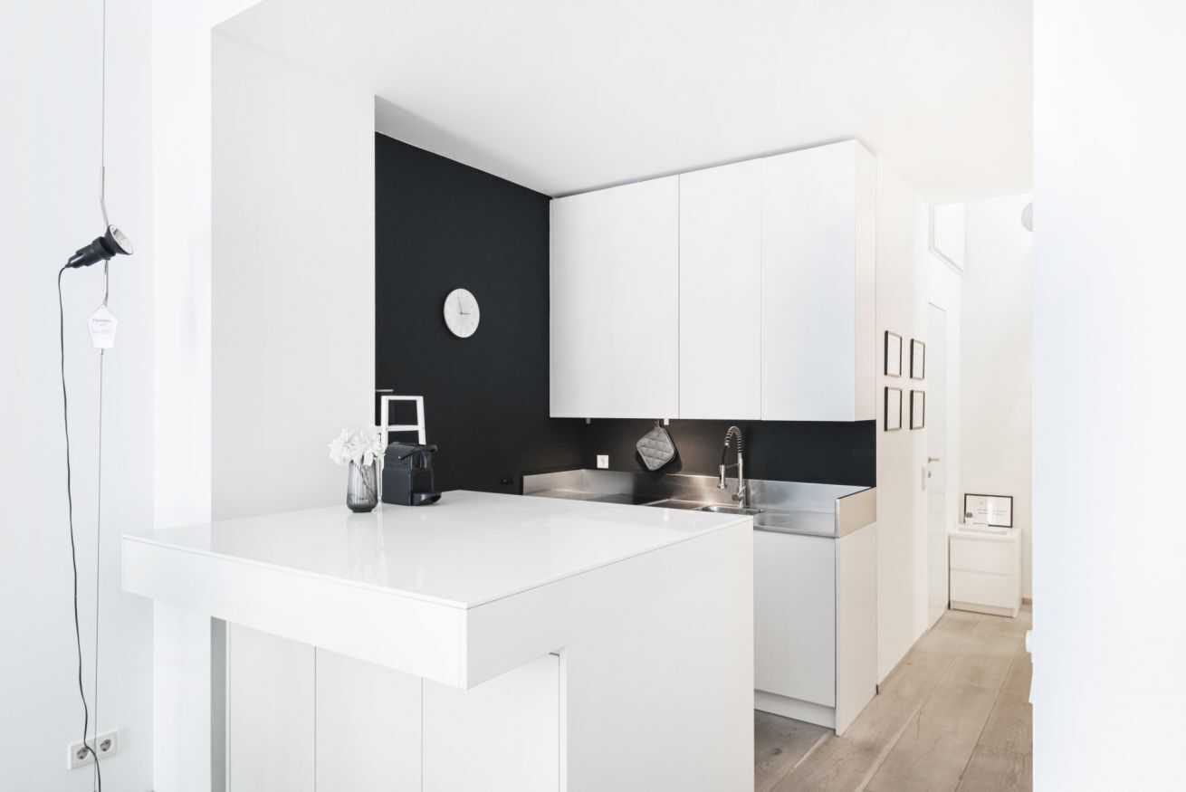 A modern kitchen with white cabinetry, a black accent wall, and a clock.