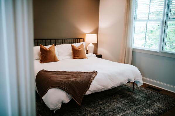 A neatly made bed with white and brown bedding, a dark patterned rug, and a bedside lamp.