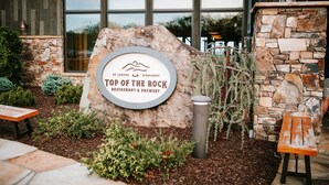 Ein Steinschild für 'Top of the Rock Restaurant & Brewery' mit einer rustikalen Steinmauer und Grünpflanzen im Vordergrund.