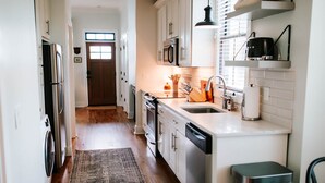 A kitchen with white cabinets, stainless steel appliances, a wooden floor, and a black trash bin. - Chic 2BR Cabin D by MHM Luxury Properties (Jasper)