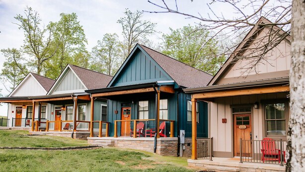 A row of cabins with individual porches, each featuring a wooden deck and a single red chair. - Chic 2BR Cabin D by MHM Luxury Properties (Jasper)