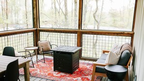 A sunroom with a view of trees, a small table, chairs, and a storage unit. - Chic 2BR Cabin D by MHM Luxury Properties (Jasper)