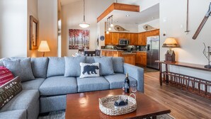 A living room with a grey sofa, a wooden coffee table, and a kitchen in the background. - Home Near Sierra Golf Course! Just a Short Walk to the Shuttle! (Mammoth Lakes)