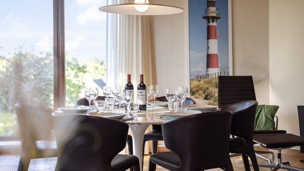 Un comedor con una mesa dispuesta para una comida, una lámpara colgante y un cuadro con una imagen de un faro.